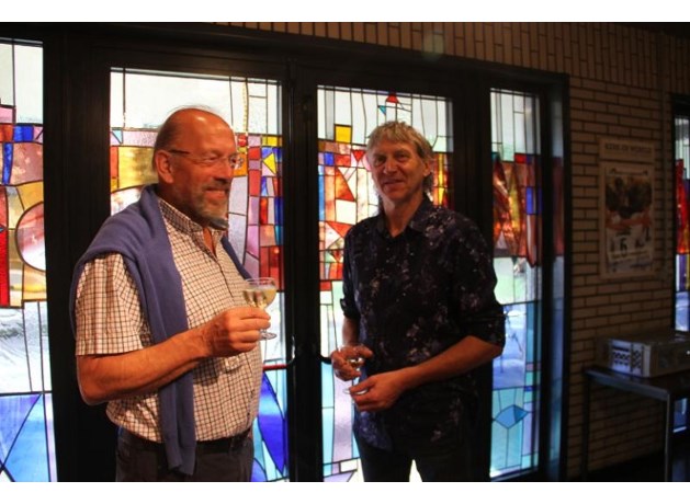 Kunstenaar-glazenier Jules Claes (links) ontwierp op vraag van de parochie Bret-Gelieren, een glas in loodraam in de te renoveren inkomhal van de Fatima Kerk. Afgelopen zondag werd het raam, na de ochtendmis, ingehuldigd met een kleine receptie. Rechts: Felicien Penders, vriend en collega-glazenier van Jules Claes en mede-uitvoerder van het kunstwerk.